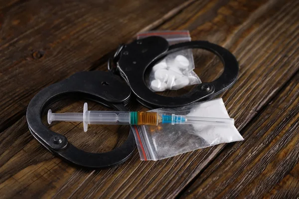 Handcuffs with a syringe drug bag symbolize drug possession charges